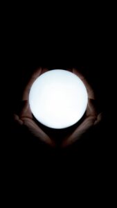 Hands holding a glowing white orb against a dark background.