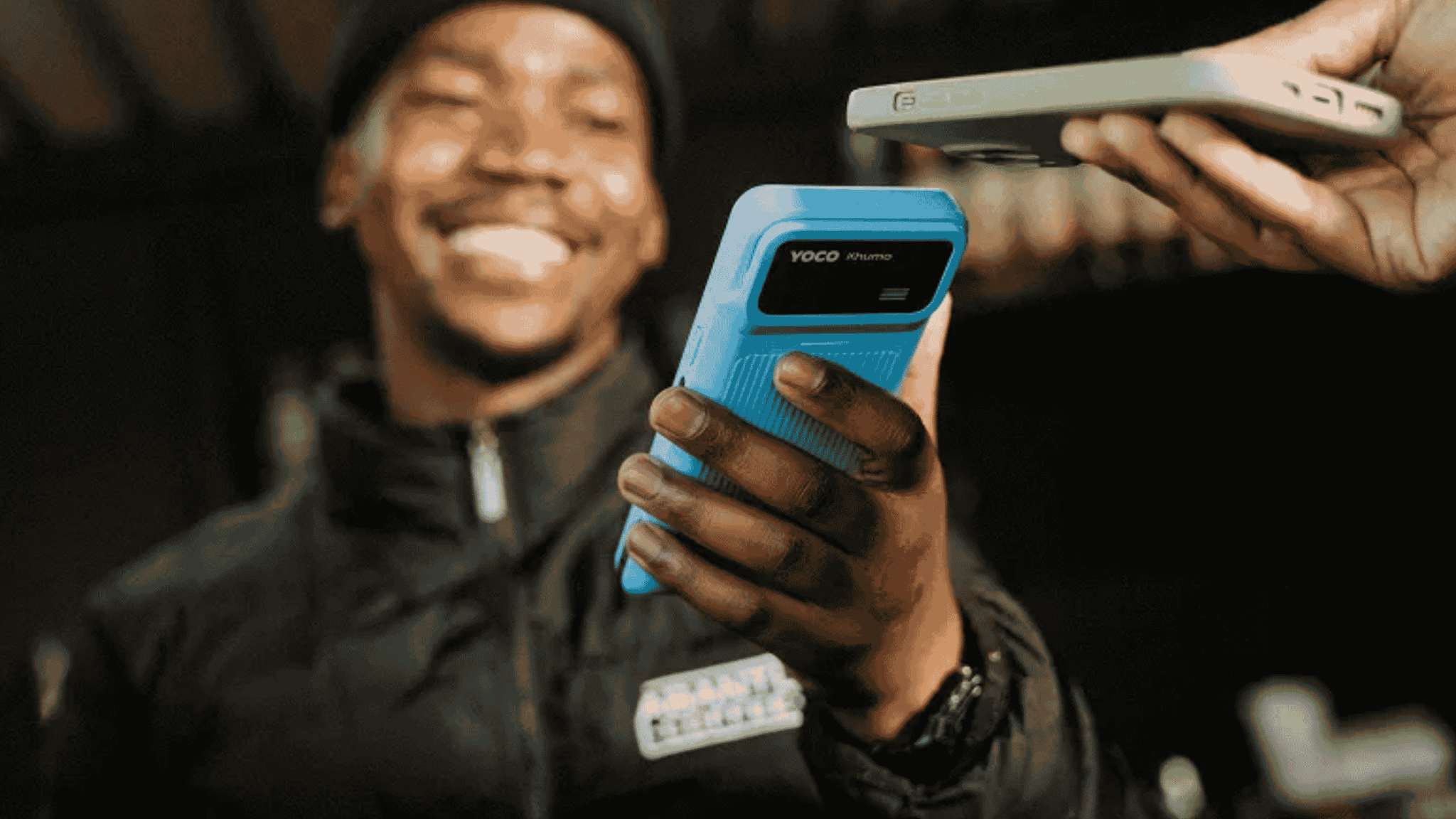 Close-up of a smiling man holding a blue Yoco Khumo card reader, tapping it against another handheld payment device.